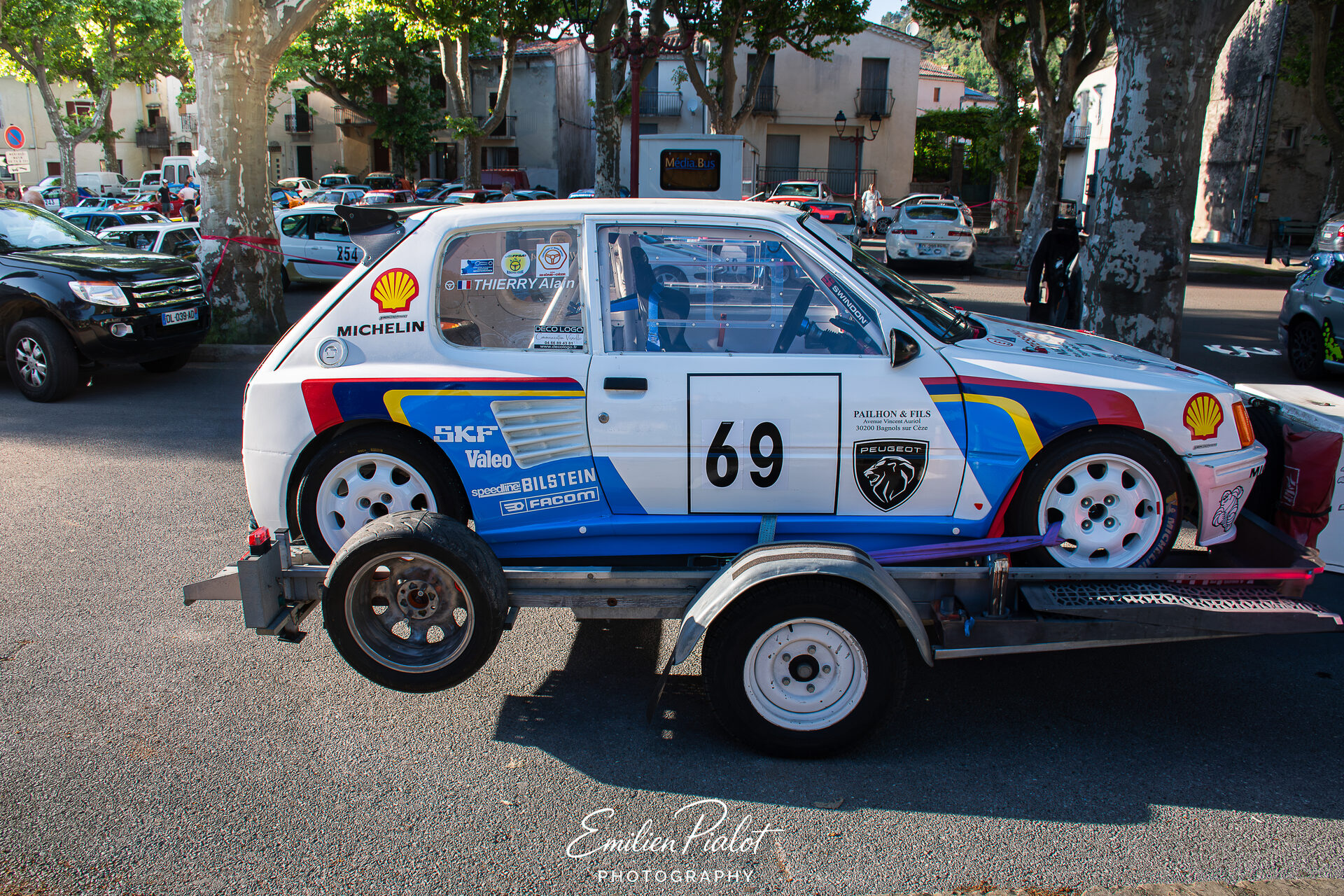 Peugeot 205 Rallye blanche et bleue sur remorque, place du village