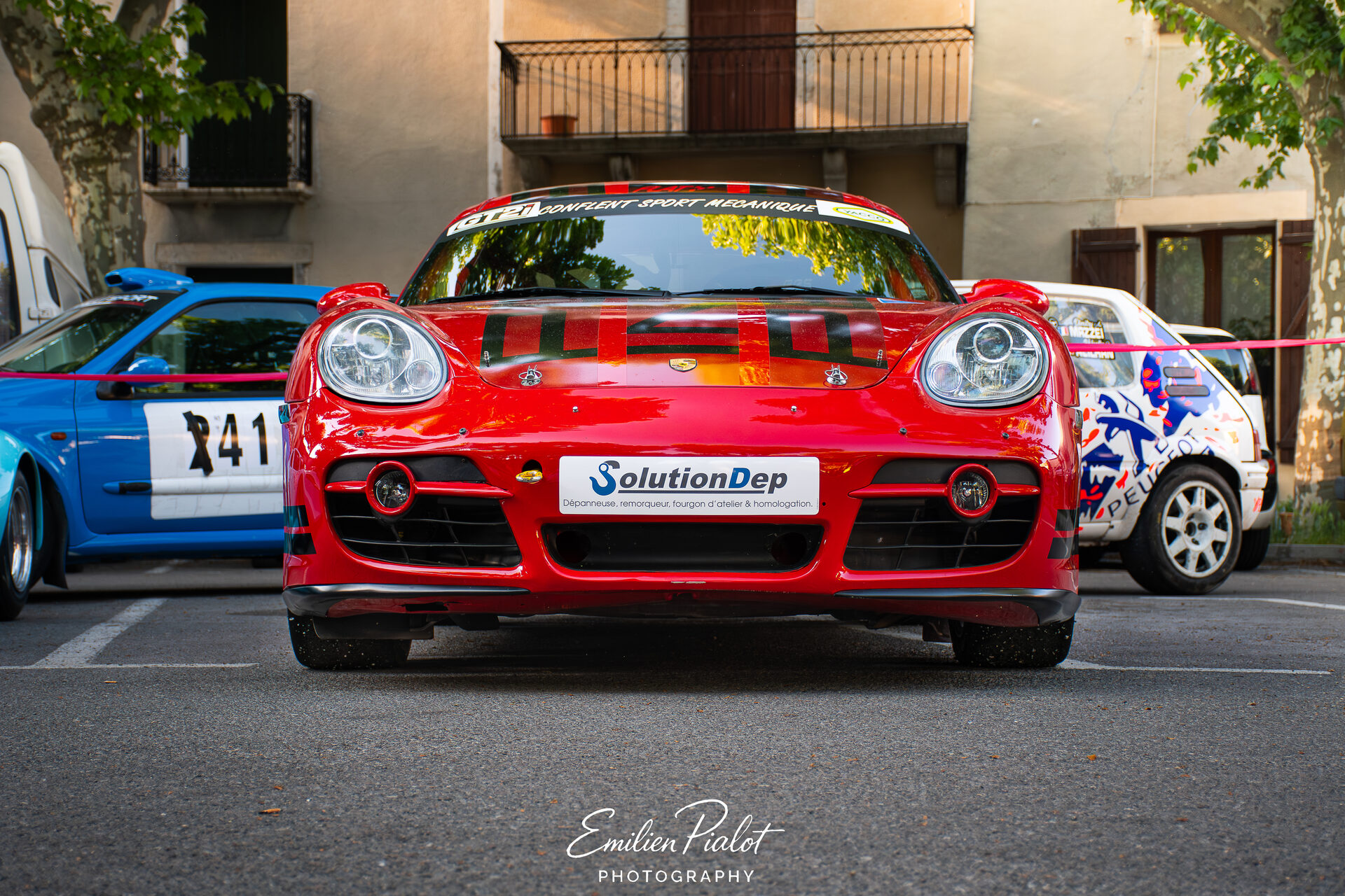 Porsche Cayman rouge vue de face, voitures alignées sur la place